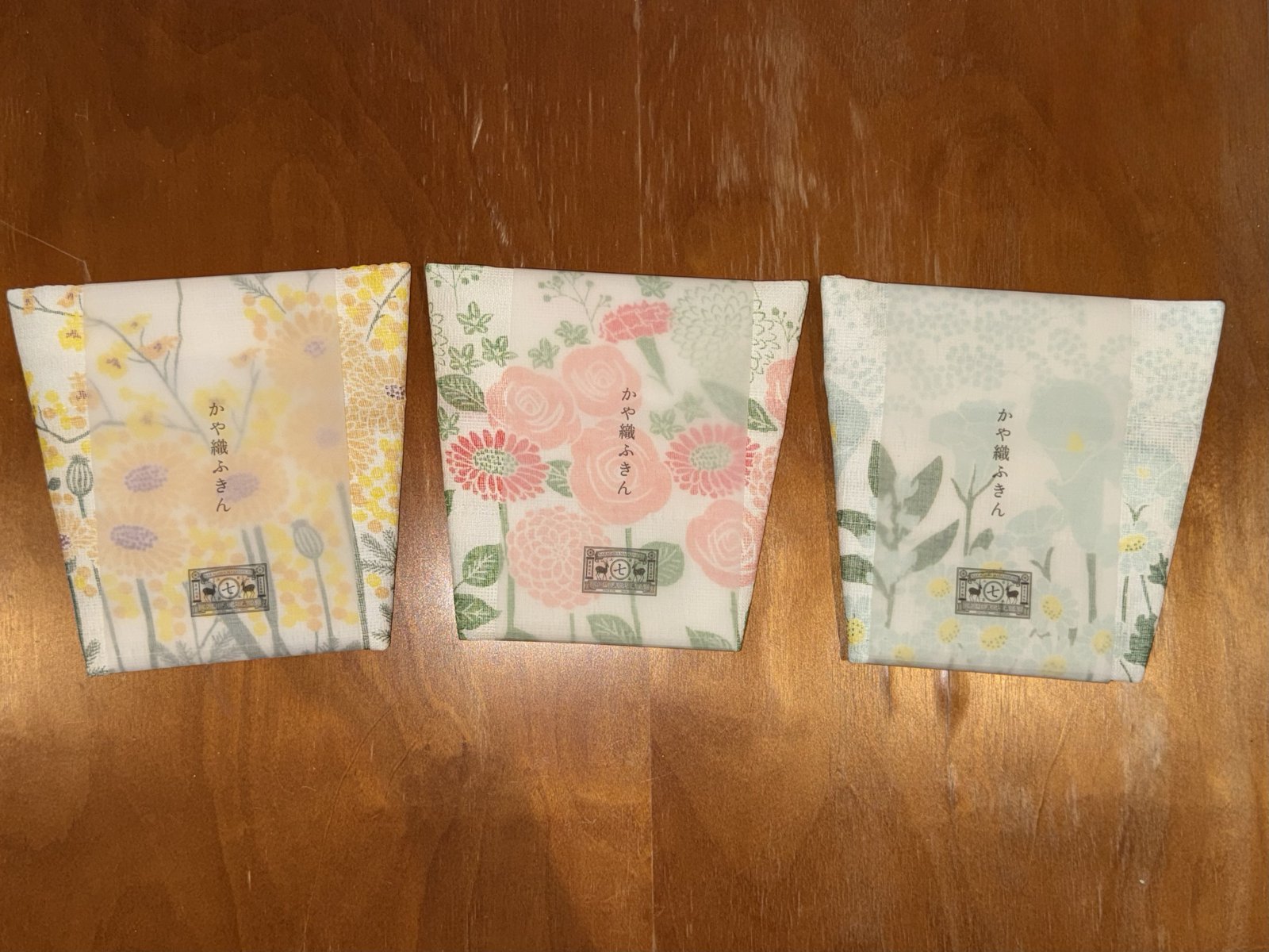 Trois torchons kayaori Nakagawa Masashichi pliés dans leur emballage, motifs mimosa, bouquet rose et marguerites