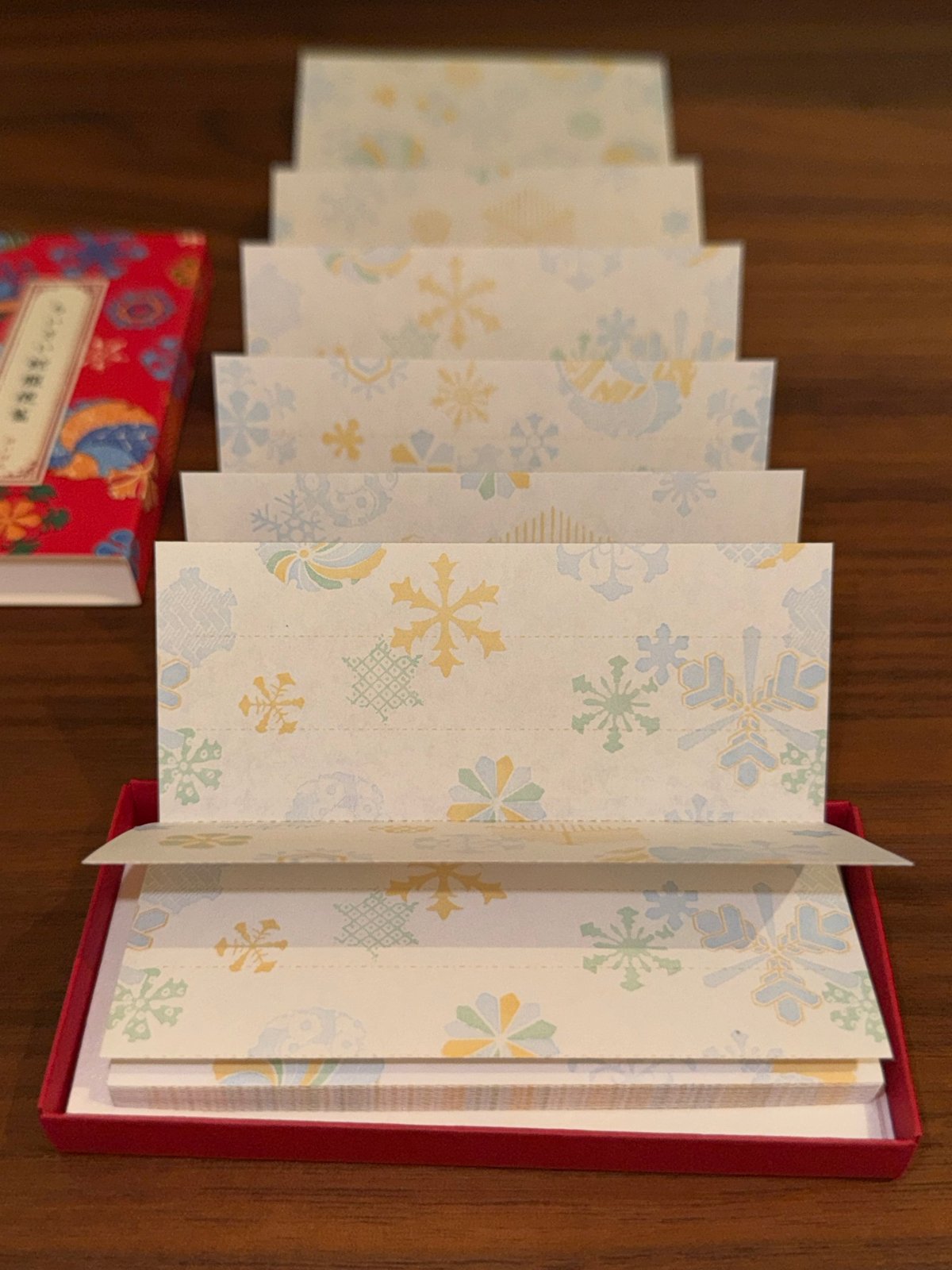 Papier à lettres accordéon Haibara déplié en zigzag hors de sa boîte rouge, motif flocons de neige pastel